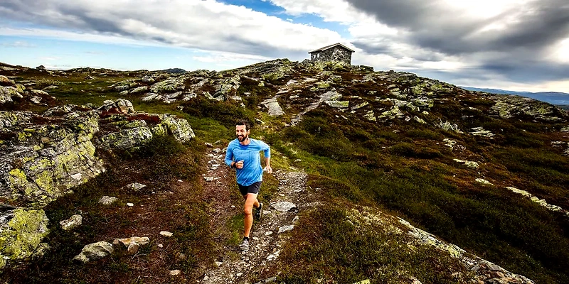 Runner on mountain trail towards stone hut. Beautiful mountain scenery. Skeikampen Up.