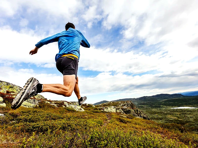 Runner jumps over terrain in the mountains. Beautiful surroundings.