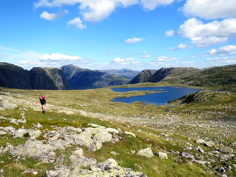 Person hiking in a mountainous landscape with lakes, clear sky.
