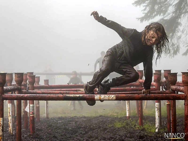 Participant climbs over an obstacle in muddy terrain during the Troll Hunter Trial in Bergen.