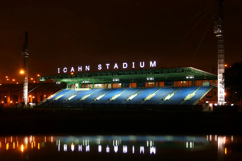 Icahn Stadium at night, with floodlights and reflections in the water.