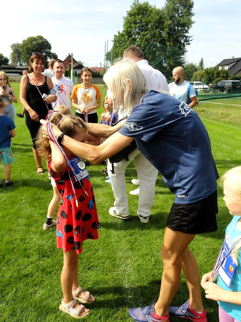 Wręczanie medalu na biegu. Dziecko otrzymuje medal. Ludzie w tle.