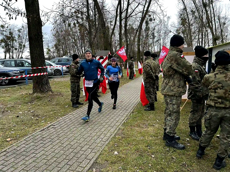 Biegacze podczas V Biegu Pamięci Powstańców Warszawy, w tle polskie flagi i żołnierze.