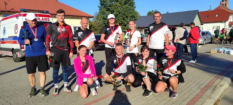 Zdjęcie grupowe biegaczy z medalami i różami po biegu.