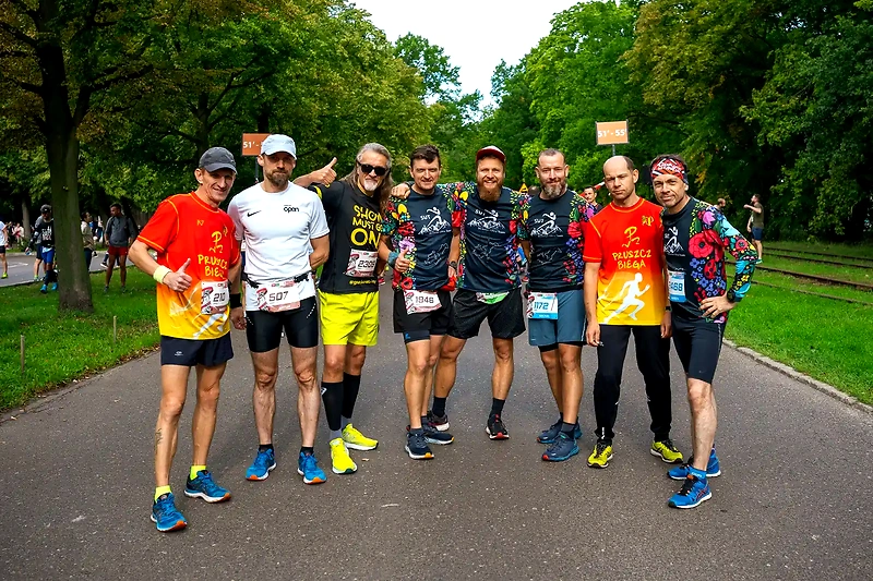 Grupa biegaczy na trasie. Widoczne numery startowe i koszulki biegowe.