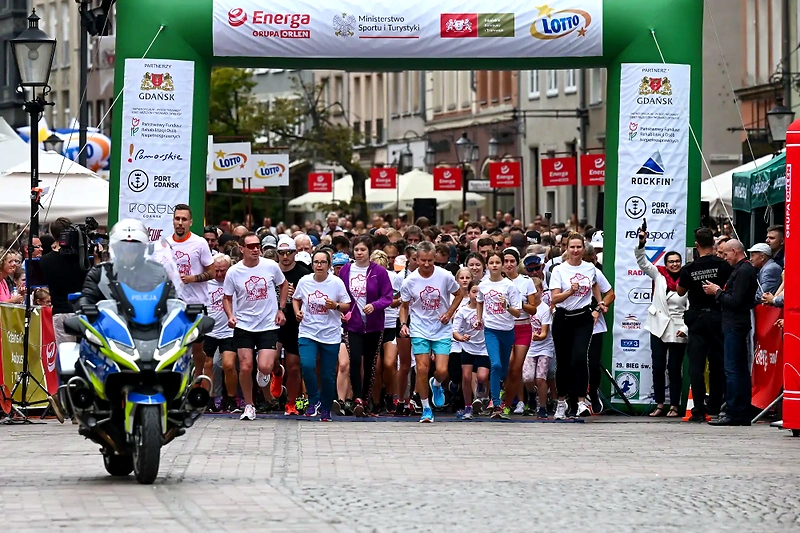 Biegacze ruszają na starcie biegu, w tle logo i sponsorzy.