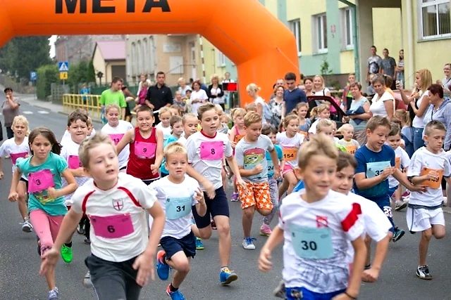 Dzieci biorą udział w biegu. Uczestnicy biegną wzdłuż ulicy.