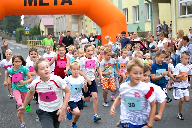 Dzieci biegną w wyścigu, pod pomarańczowym łukiem z napisem META.
