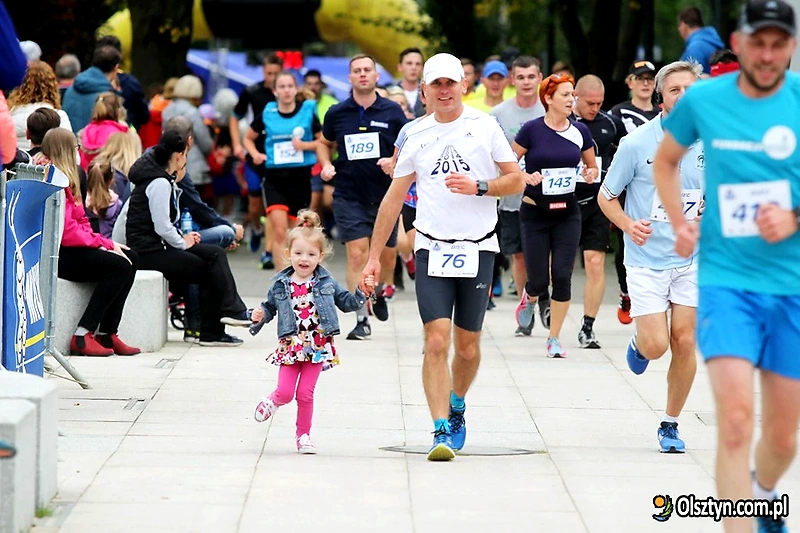 Runners during the competition, including a child holding an adult's hand. People are cheering.