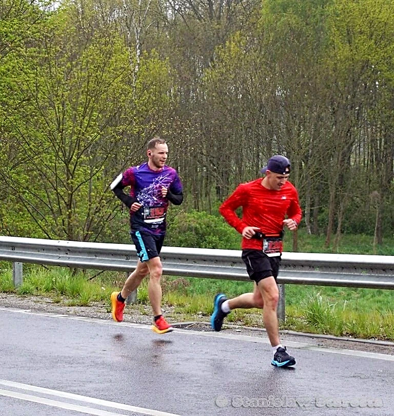 Dwóch biegaczy podczas biegu w deszczu, na tle lasu.