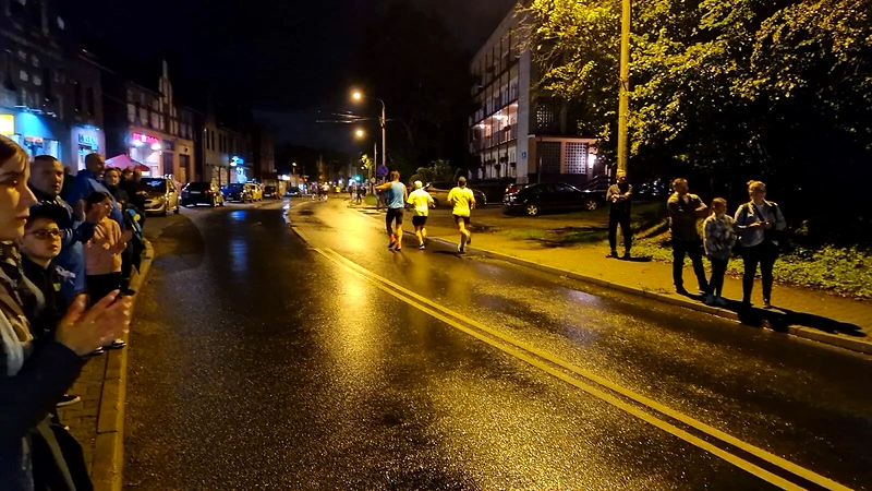 Biegacze nocnego biegu ulicznego w Czerwionce-Leszczynach, wzdłuż mokrej drogi.