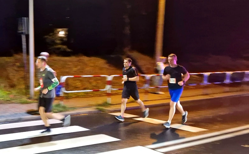 Zawodnicy biegną w nocnym biegu ulicznym.