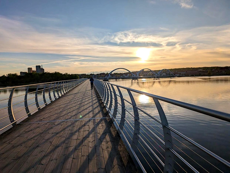 A person walks on a bridge at sunset.