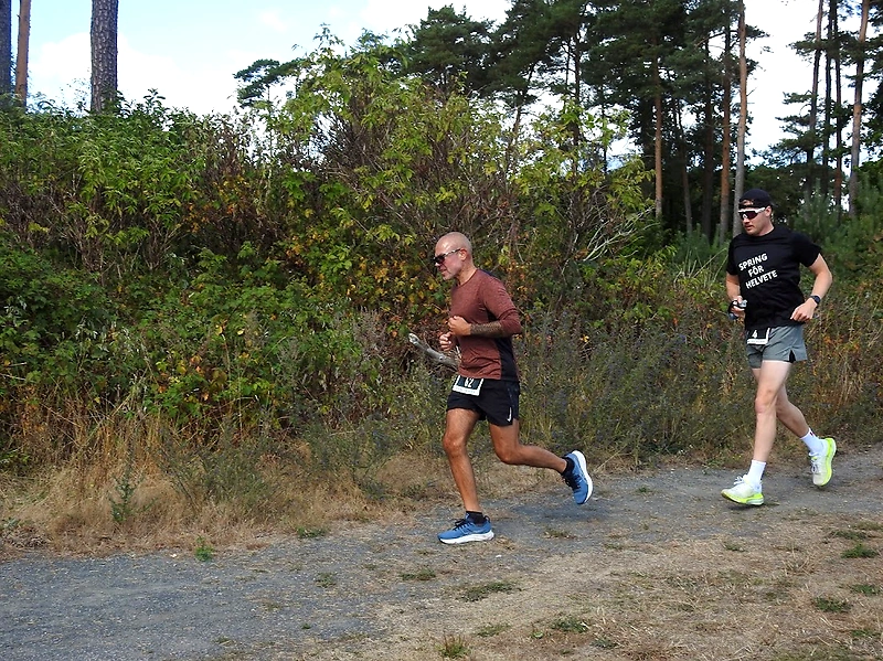 Två löpare på en grusväg under ett lopp, omgivna av grönska och träd.