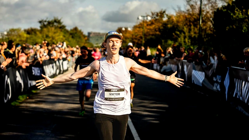 Löpare korsar mållinjen i Malmö Marathon med armarna utsträckta, publiken hejar på.