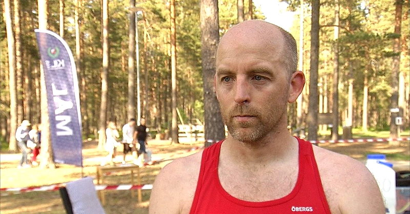 Löpare i röd tröja i skogen vid ett evenemang med andra människor.