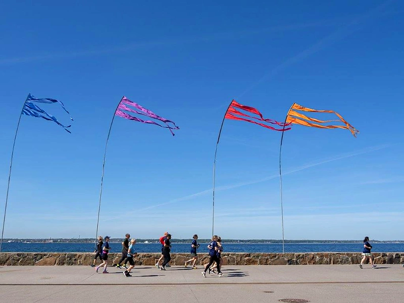 Löpare vid vattnet med färgglada flaggor i bakgrunden.