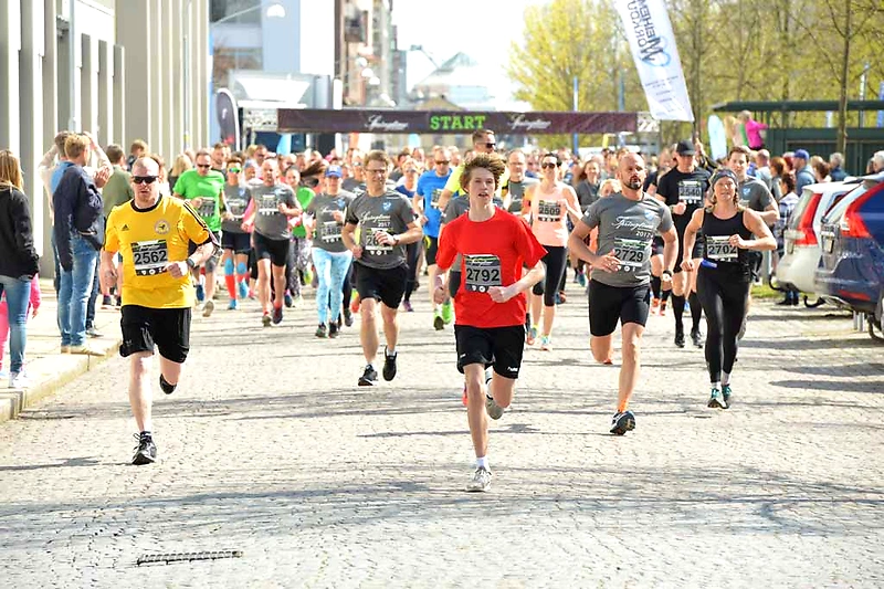 Deltagare springer i ett lopp med publik och startskyltar i bakgrunden.