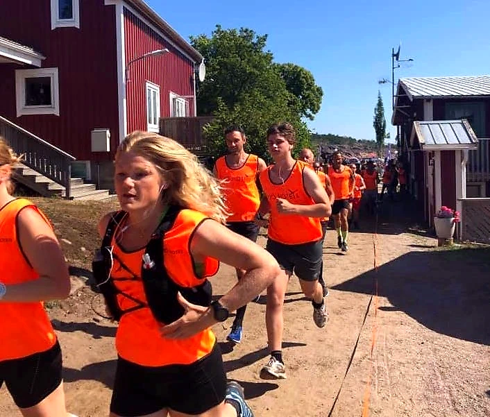 Löpare i orange västar springer i en tävling.