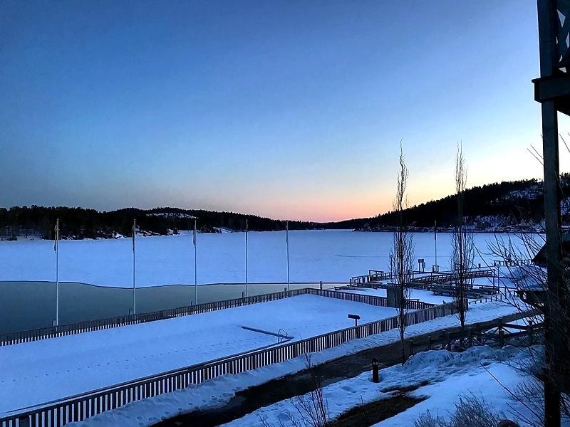 Vintervy över Ulvön, snö, vatten och träd i solnedgången.