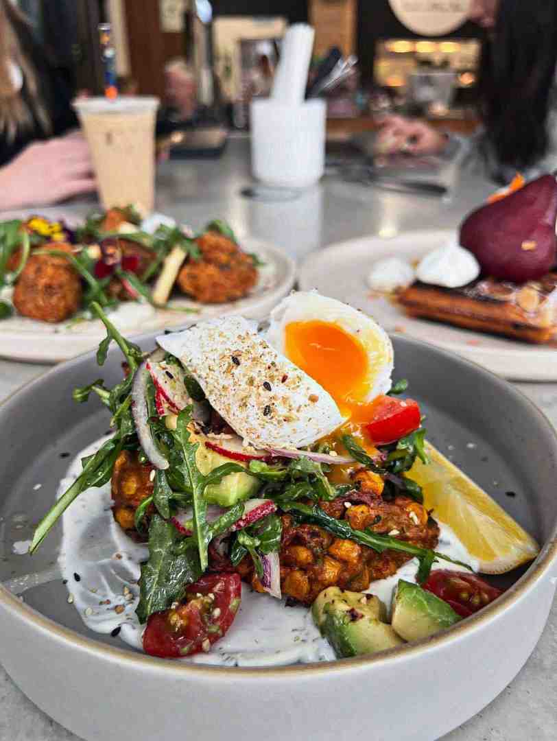 Corn Fritters dish with poached egg, avocado, and fresh herbs - all day brekky