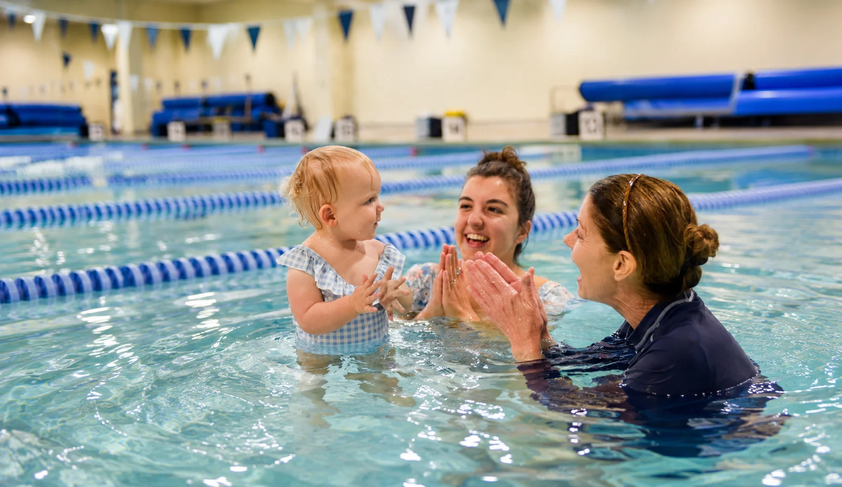 Small infant swim class led by a smiling swim instructor in a warm pool Small infant swim class led by a smiling swim instructor in a warm pool
