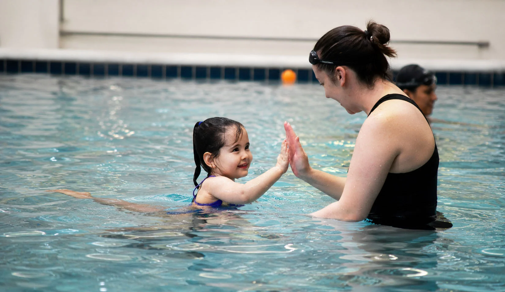 Instructor teaching a young child swimming fundamentals in a warm indoor pool Instructor teaching a young child swimming fundamentals in a warm indoor pool