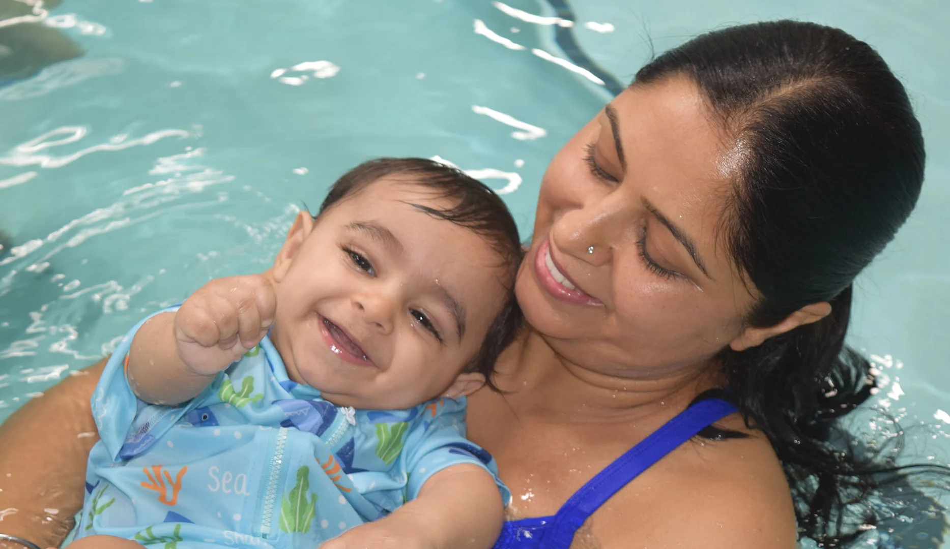 Parent and baby smiling together in a warm indoor swim class Parent and baby smiling together in a warm indoor swim class