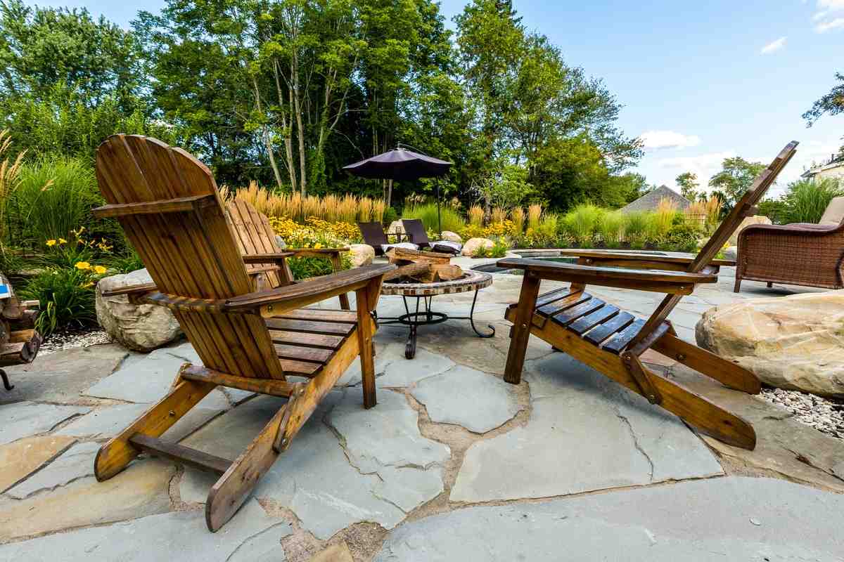 A custom stone patio with a built-in fire pit, surrounded by lush green landscaping in a backyard setting. - Georgetown MA landscape design A custom stone patio with a built-in fire pit, surrounded by lush green landscaping in a backyard setting. - Georgetown MA landscape design