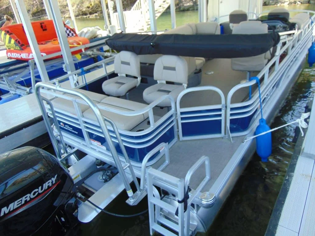 A pontoon boat on a calm lake with family and dogs swimming