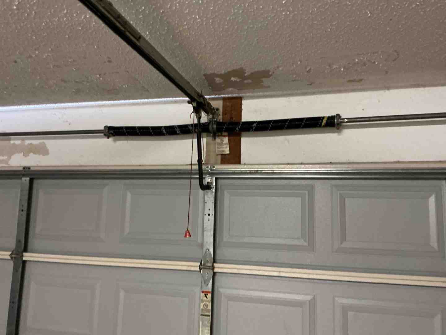 Infographic showing the complete garage door system breakdown: torsion springs at the top that counterbalance door weight, lift cables running along both sides connected to cable drums, multiple rollers on each side that guide the door along metal tracks, horizontal and vertical track sections, safety sensors at the bottom on each side, and the garage door opener motor unit mounted to the ceiling with a rail connecting to the door via an arm, plus weatherstripping along all edges for insulation and pest control - garage door installation repair near me in cedar park tx