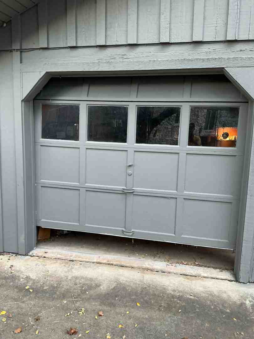 A close-up image of a garage door track with a noticeable bend, causing the roller to be out of alignment and potentially jamming the door - garage door maintenance in lakeway tx