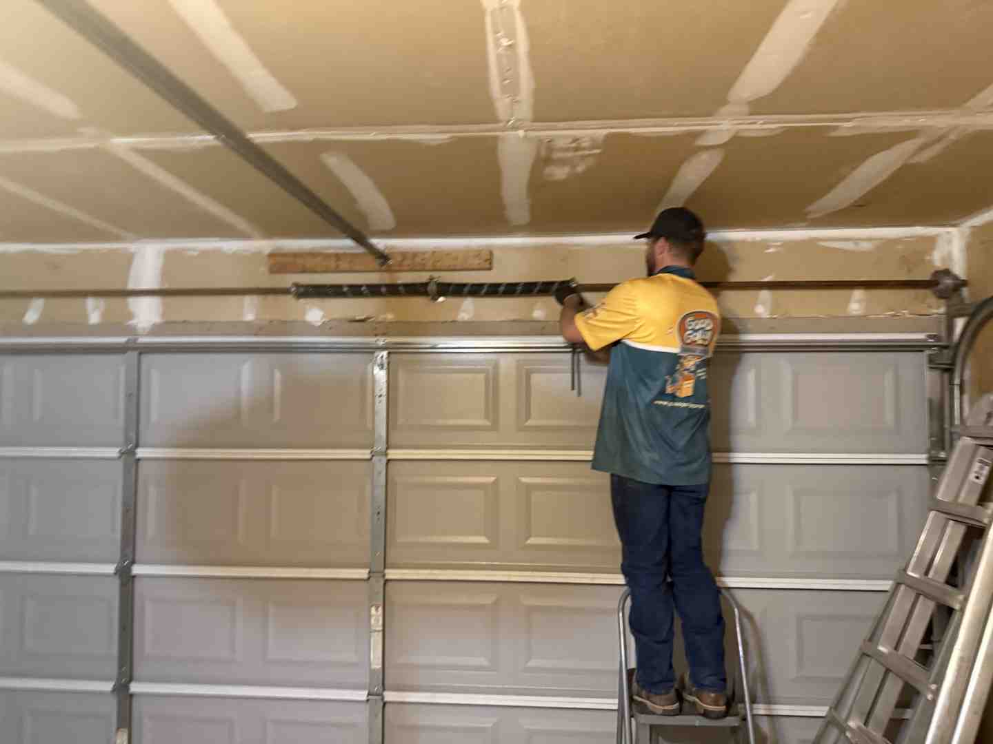Technician inspecting a high-tension torsion spring system above a garage door - broken garage door spring emergency in Technician inspecting a high-tension torsion spring system above a garage door - broken garage door spring emergency in