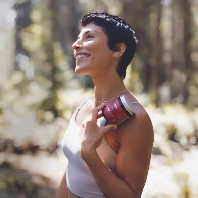 A smiling woman outdoors holding a jar of "Energize Now" capsules, a premium choice for organic mushroom supplements. A smiling woman outdoors holding a jar of "Energize Now" capsules, a premium choice for organic mushroom supplements.