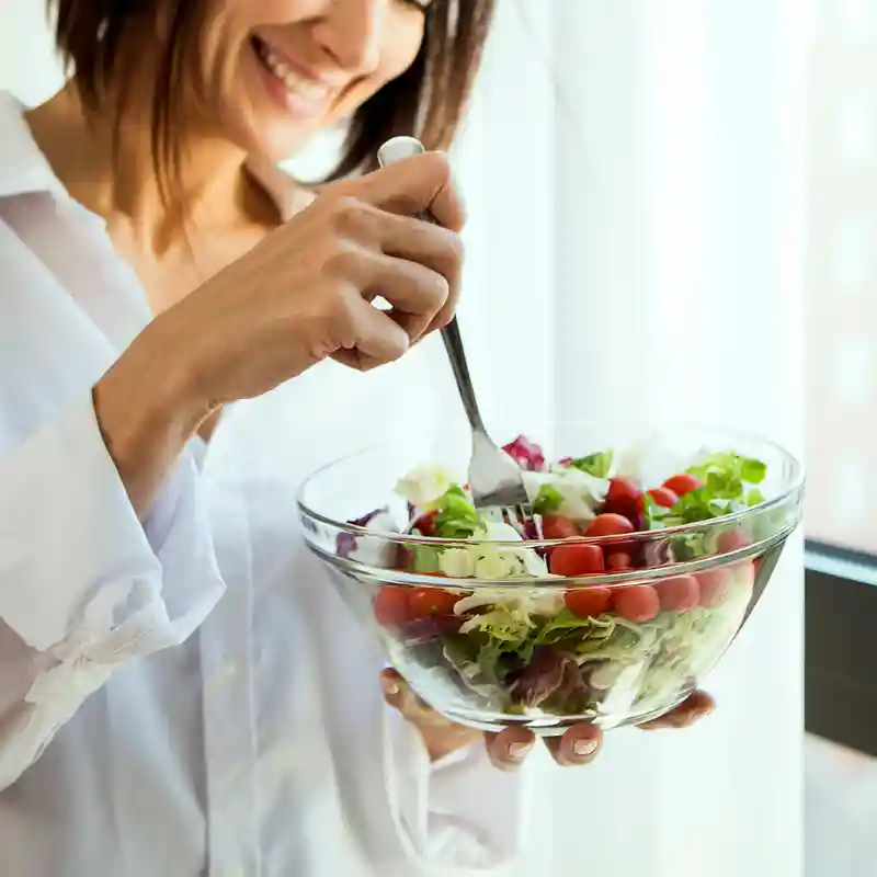 A smiling woman eating a large, fresh salad of leafy greens and tomatoes for a natural, vitamin-rich daily immune boost. A smiling woman eating a large, fresh salad of leafy greens and tomatoes for a natural, vitamin-rich daily immune boost.