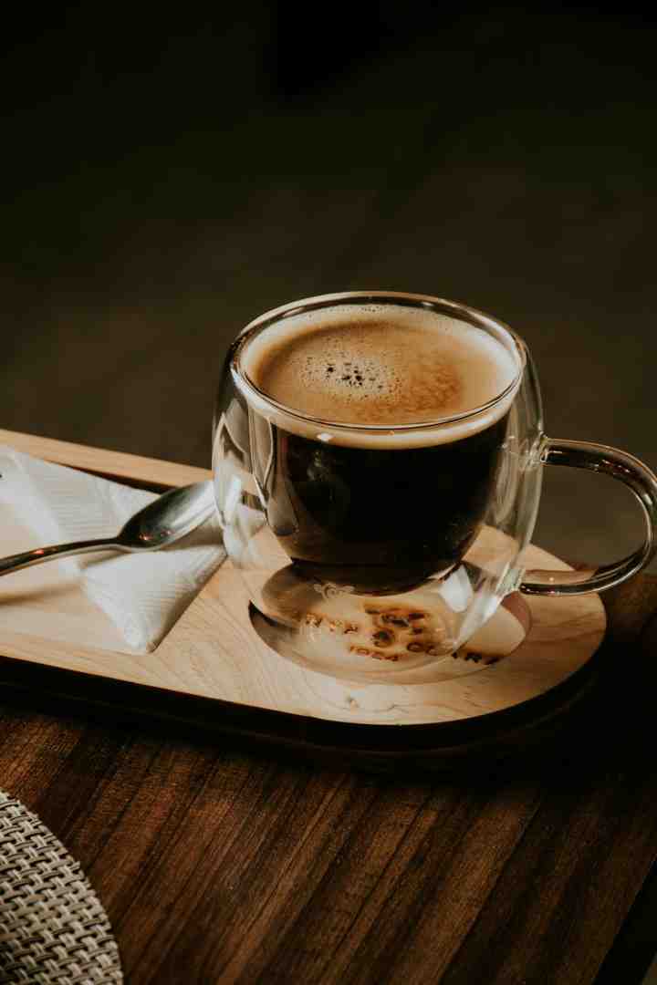 Cup of brewed coffee next to coffee beans and a spoon - caffeine content in coffee roasts