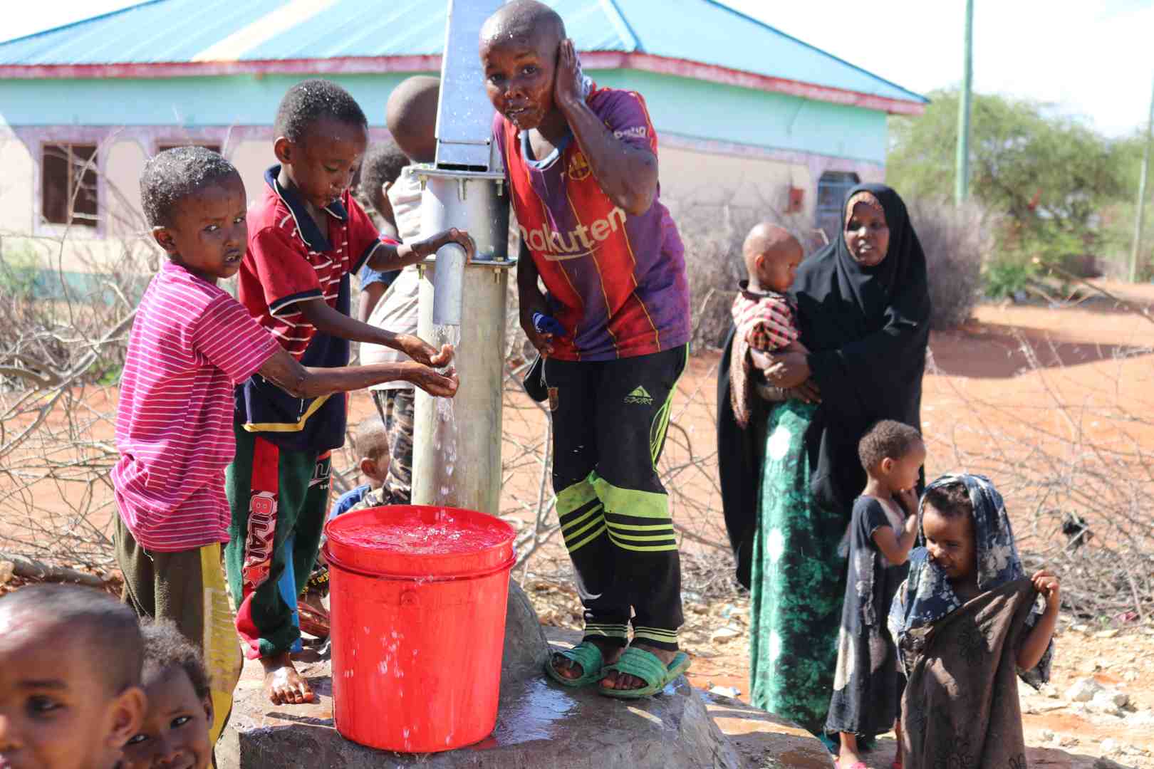A vibrant community celebrating around a newly constructed water well, with children playing and adults drawing clean water, symbolizing the life-changing impact of such projects - how to give sadaqah