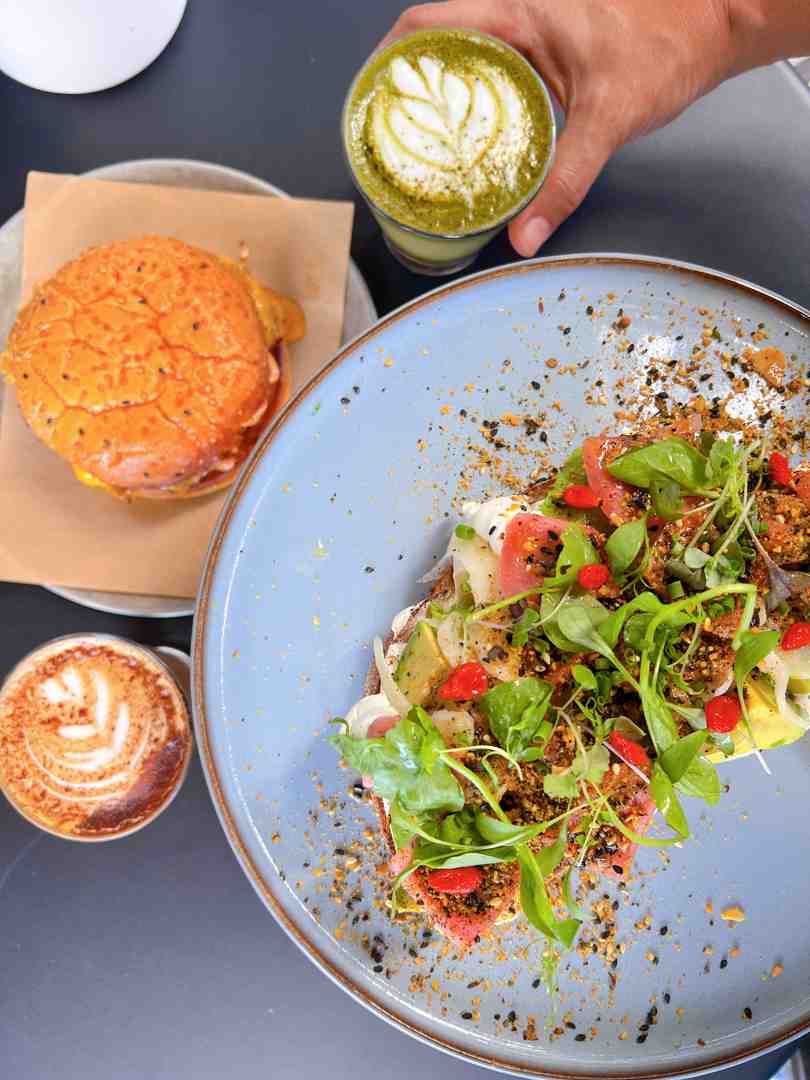 A Flat White coffee with latte art next to breakfast.
