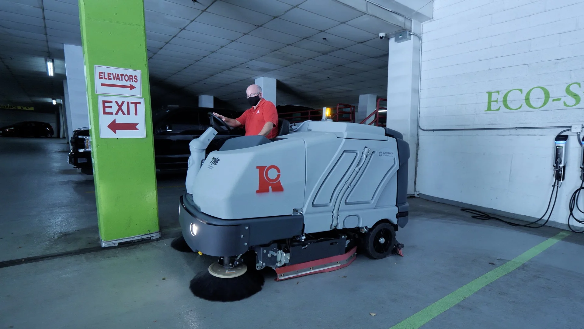 cleaner in red shirt and black pants operating a ride-on floor scrubber