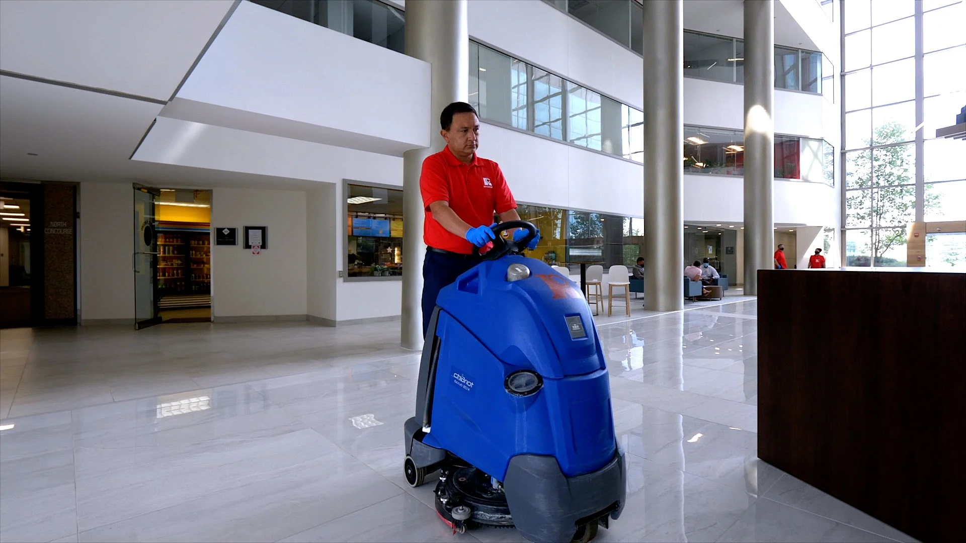 cleaner in red shirt and black pants using a floor scrubber