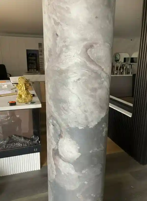 A structural column wrapped in flexible stone faux wall panels with a grey marble texture in a modern showroom.