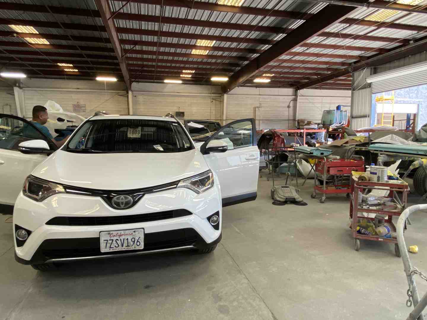 friendly technician inspecting a car's paintwork in a clean auto body shop - car scratch repair near me