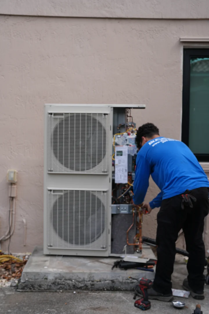 A technician performing a residential AC tune-up, checking the outdoor unit's components