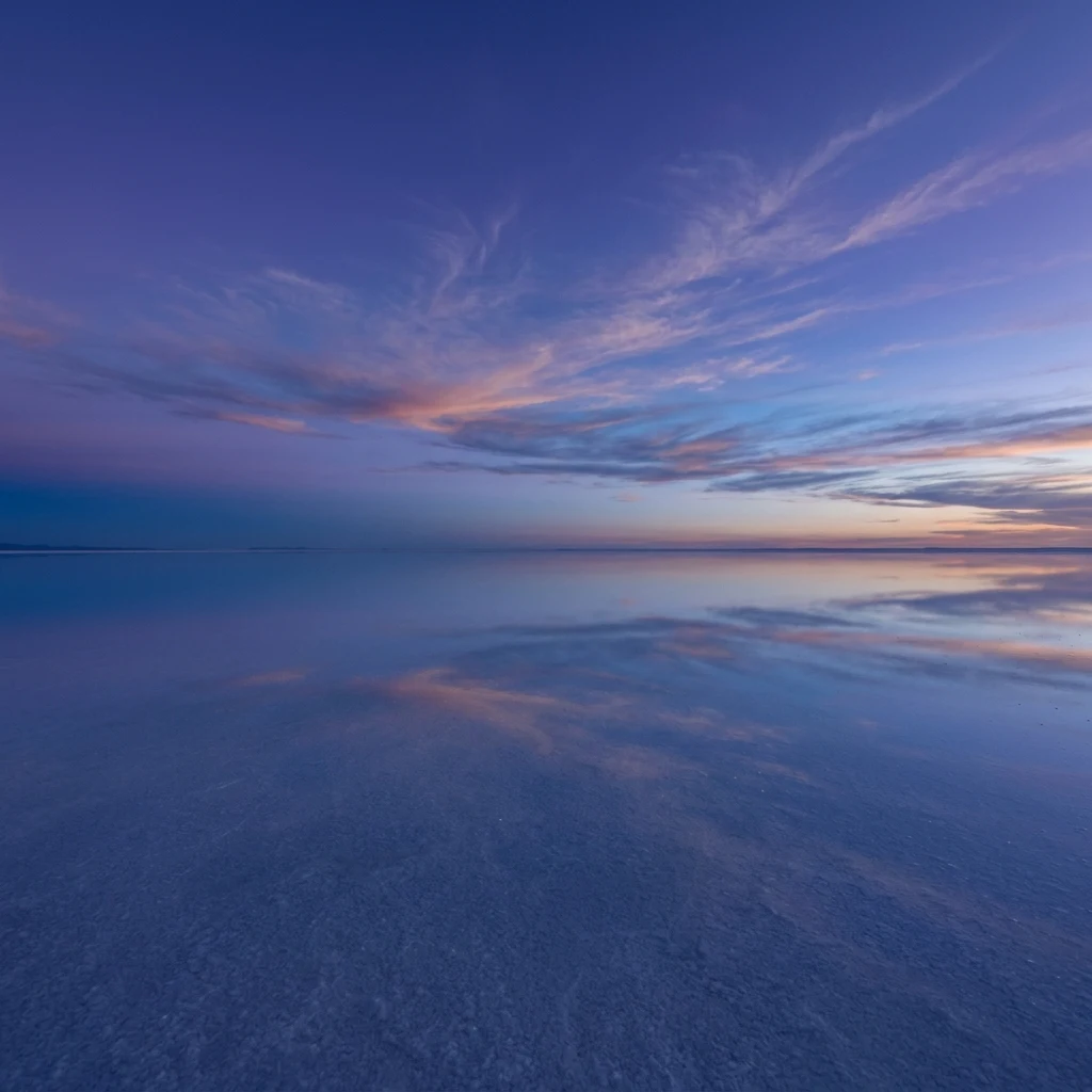 A vast salt flat in the Salar de Uyuni reflecting a violet blue hour sky after a light…