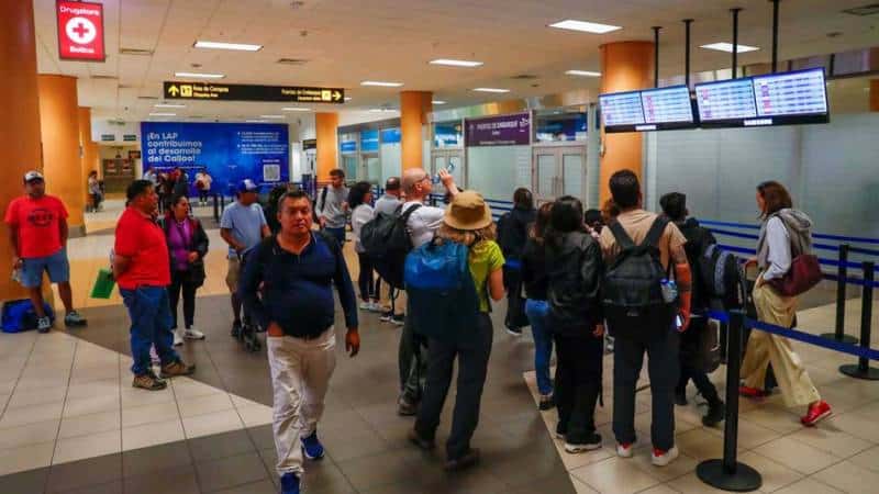 Pasajeros en proceso de facturación con pantallas de vuelos visibles