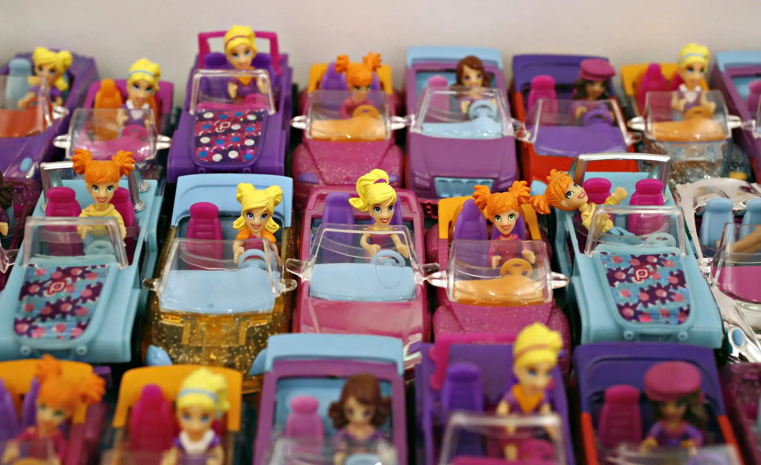 Muñecas con cabello colorido conduciendo autos de juguete alineados en filas
