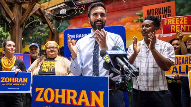 Zohran Mamdani en mitin electoral con carteles de campaña