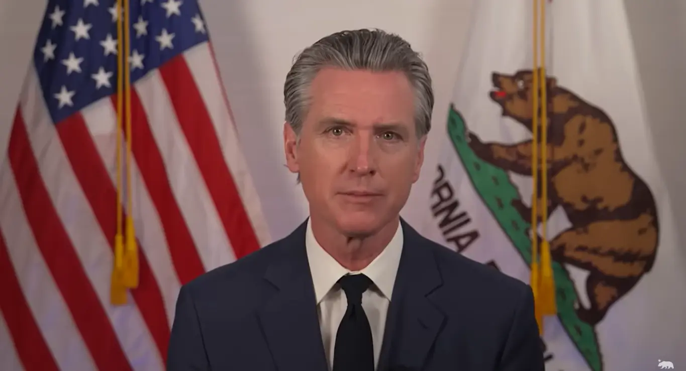 Gavin Newsom sentado formalmente con banderas de EE.UU. y California