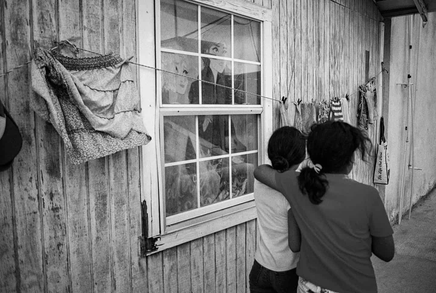 Dos ni&ntilde;as abraz&aacute;ndose observando through una ventana