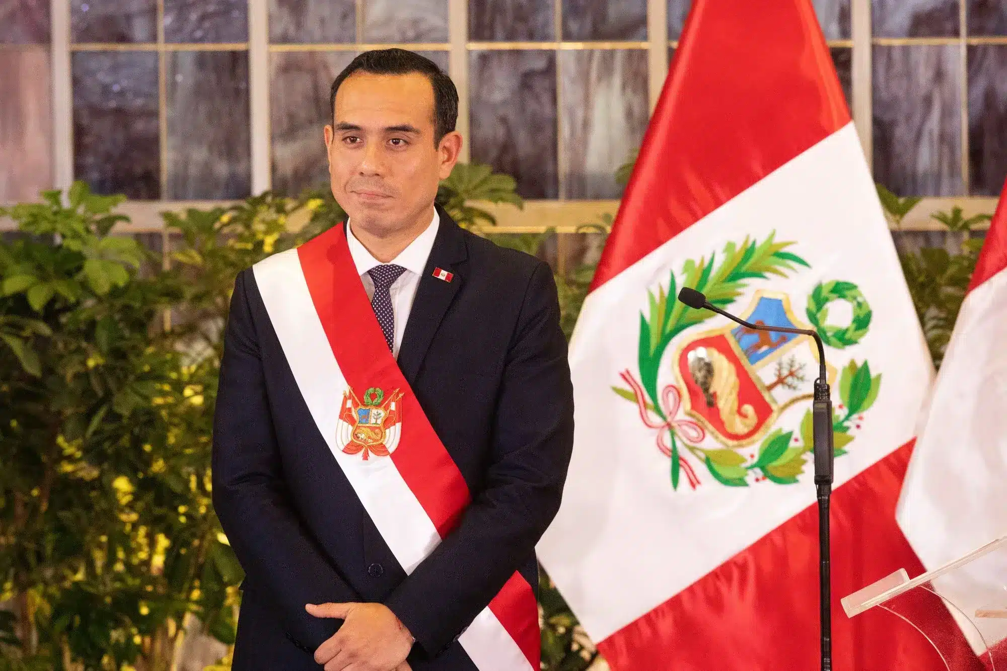 Hombre con traje oscuro y banda presidencial peruana en entorno formal